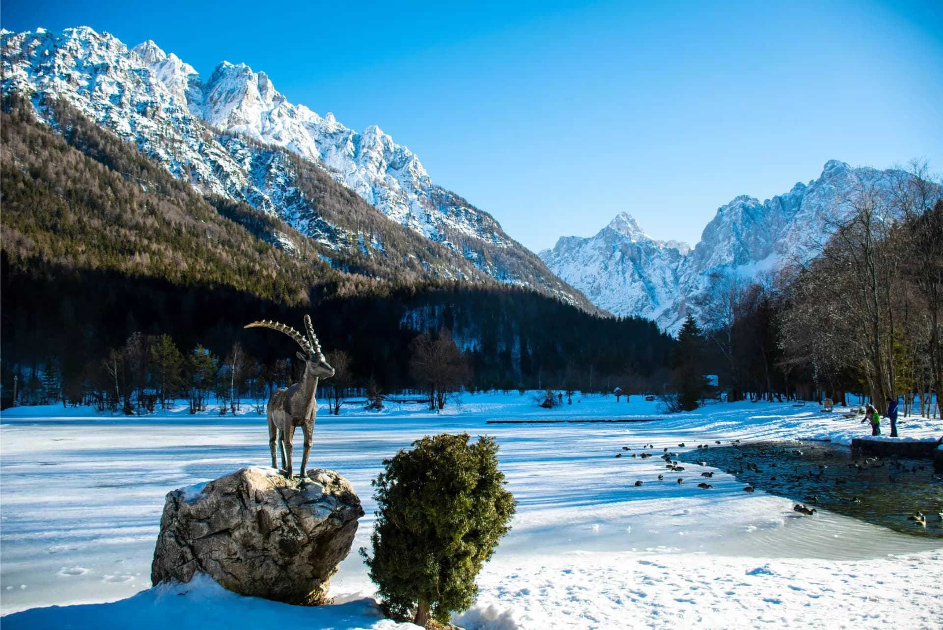 Ibex statue by frozen Lake Jasna with snow-covered Julian Alps in winter.