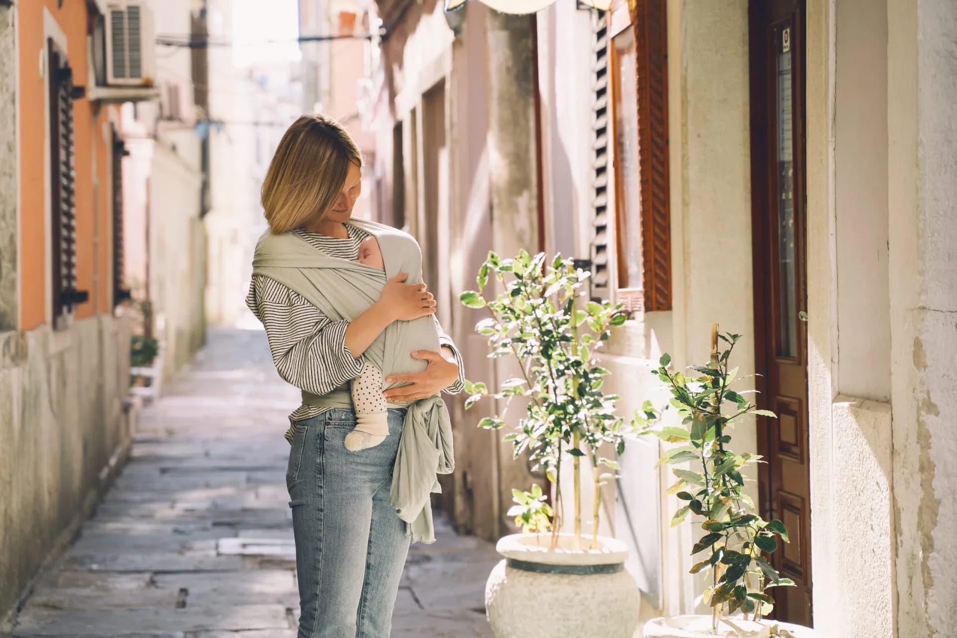 Mother babywearing in sling on sunny stone alley in Piran, Slovenia