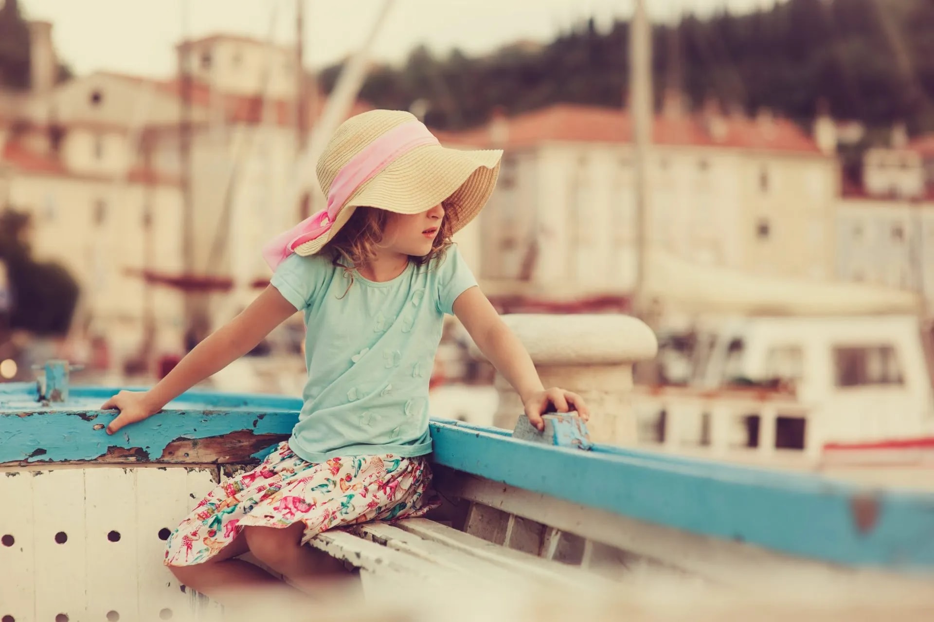 Girl in straw hat sitting in boat with harbor town background in Piran
