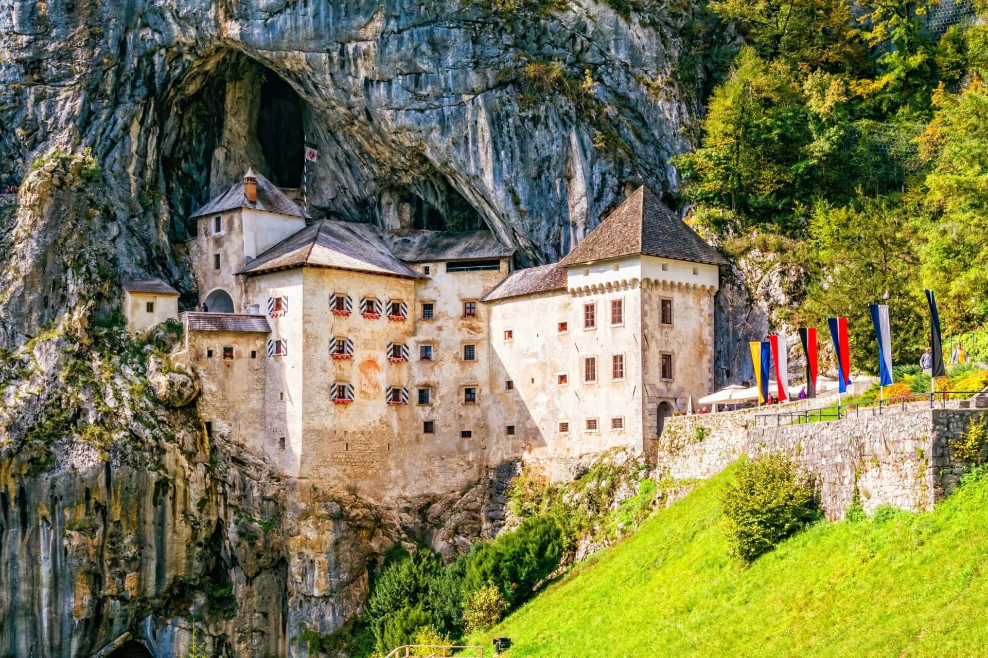 Predjama Castle built into a cliff face with green hillside and colorful flags.