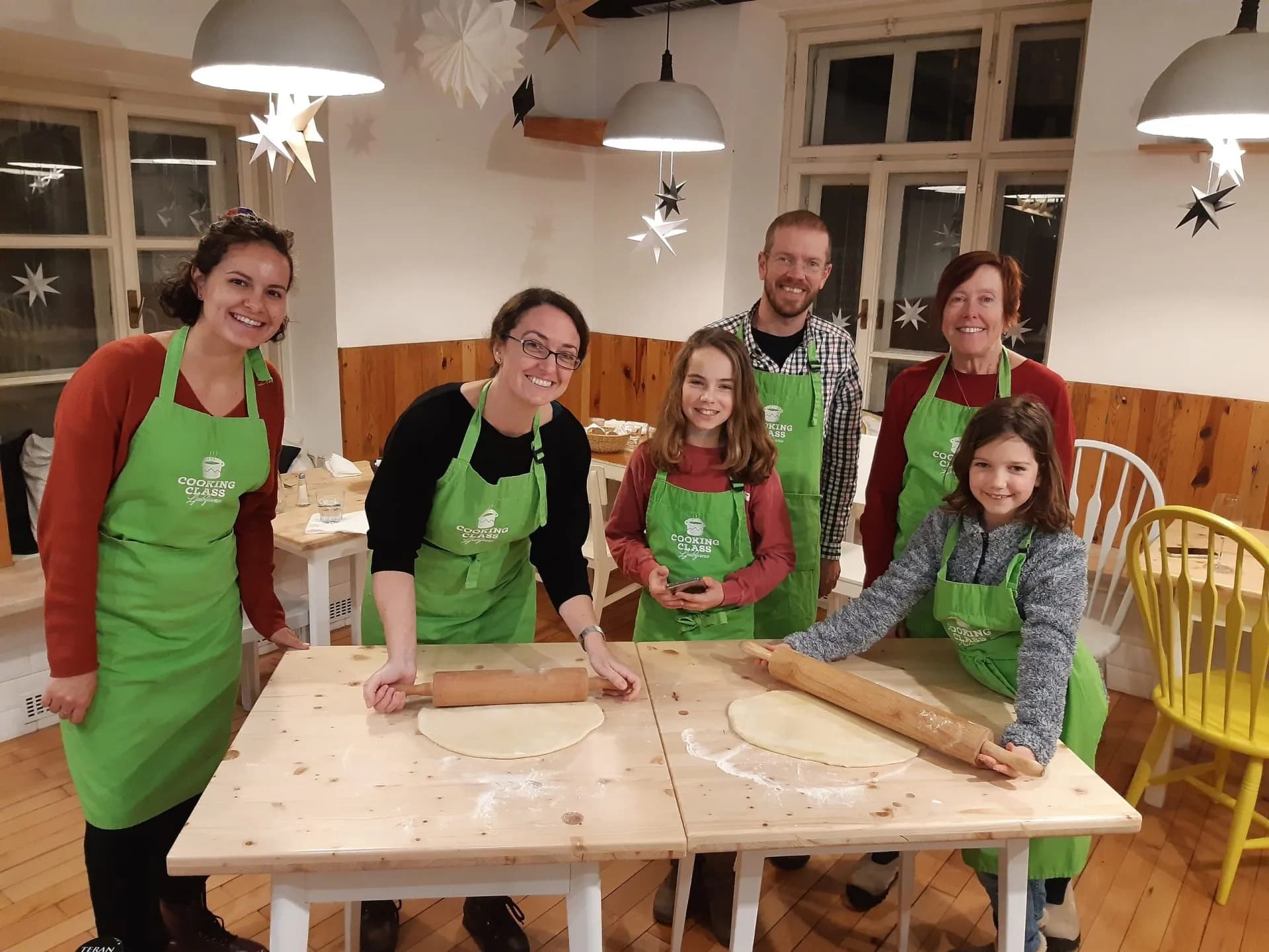 Family group rolling dough with rolling pins during a cooking class in Ljubljana.