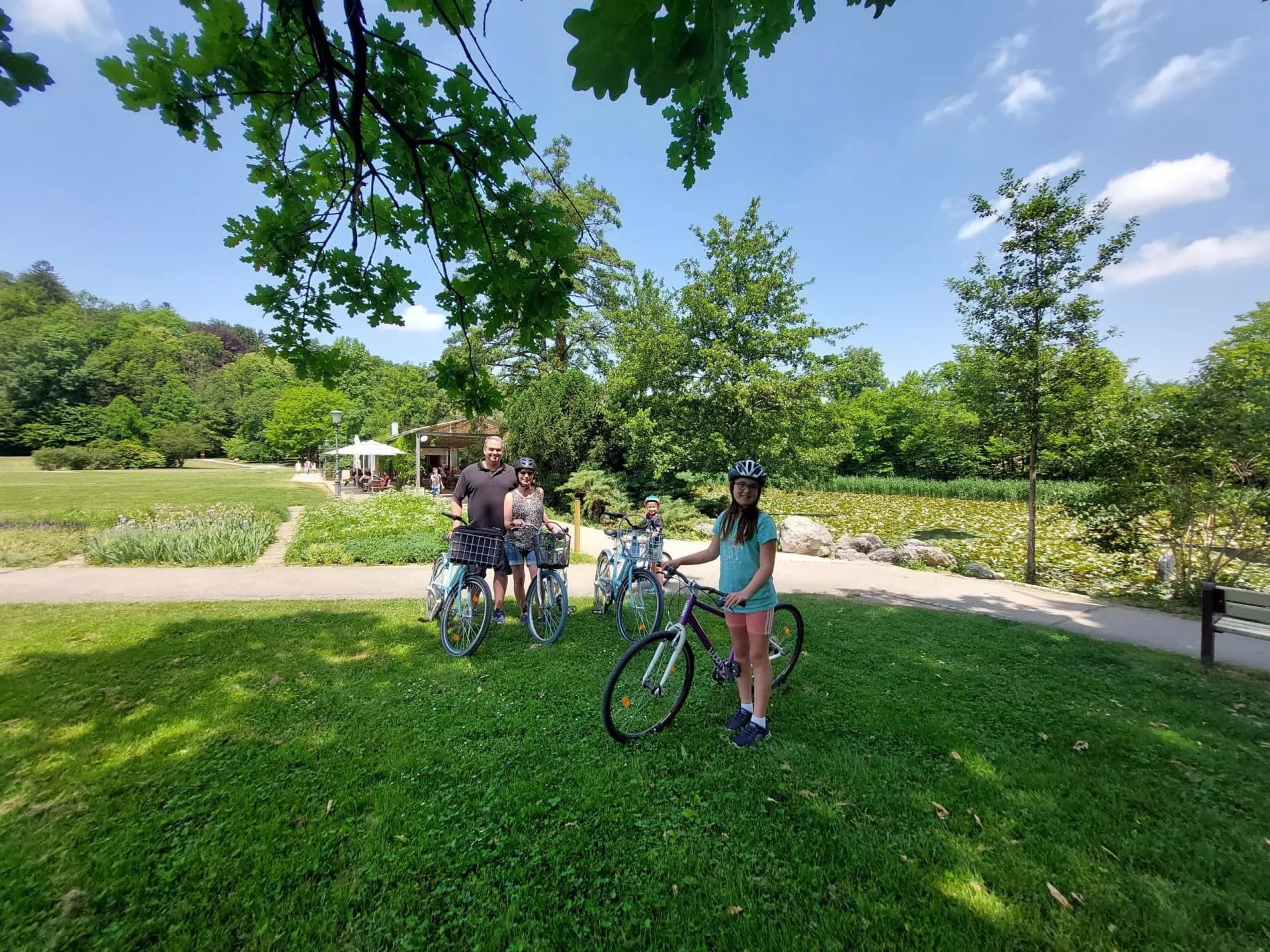 Family with bicycles on grass near pond in park, Tivoli in filename.