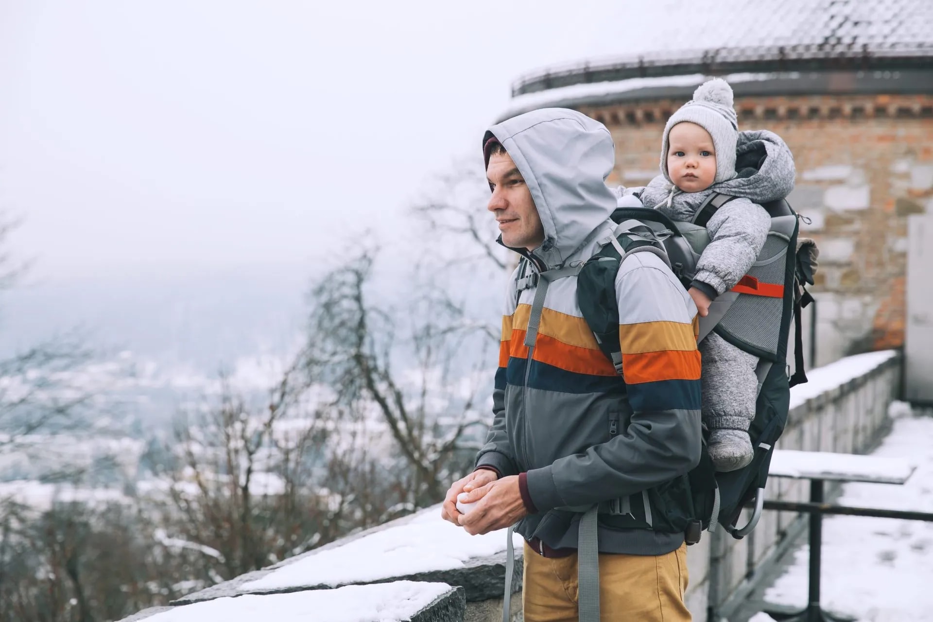 Father carrying baby in carrier outdoors in Ljubljana during winter with snow