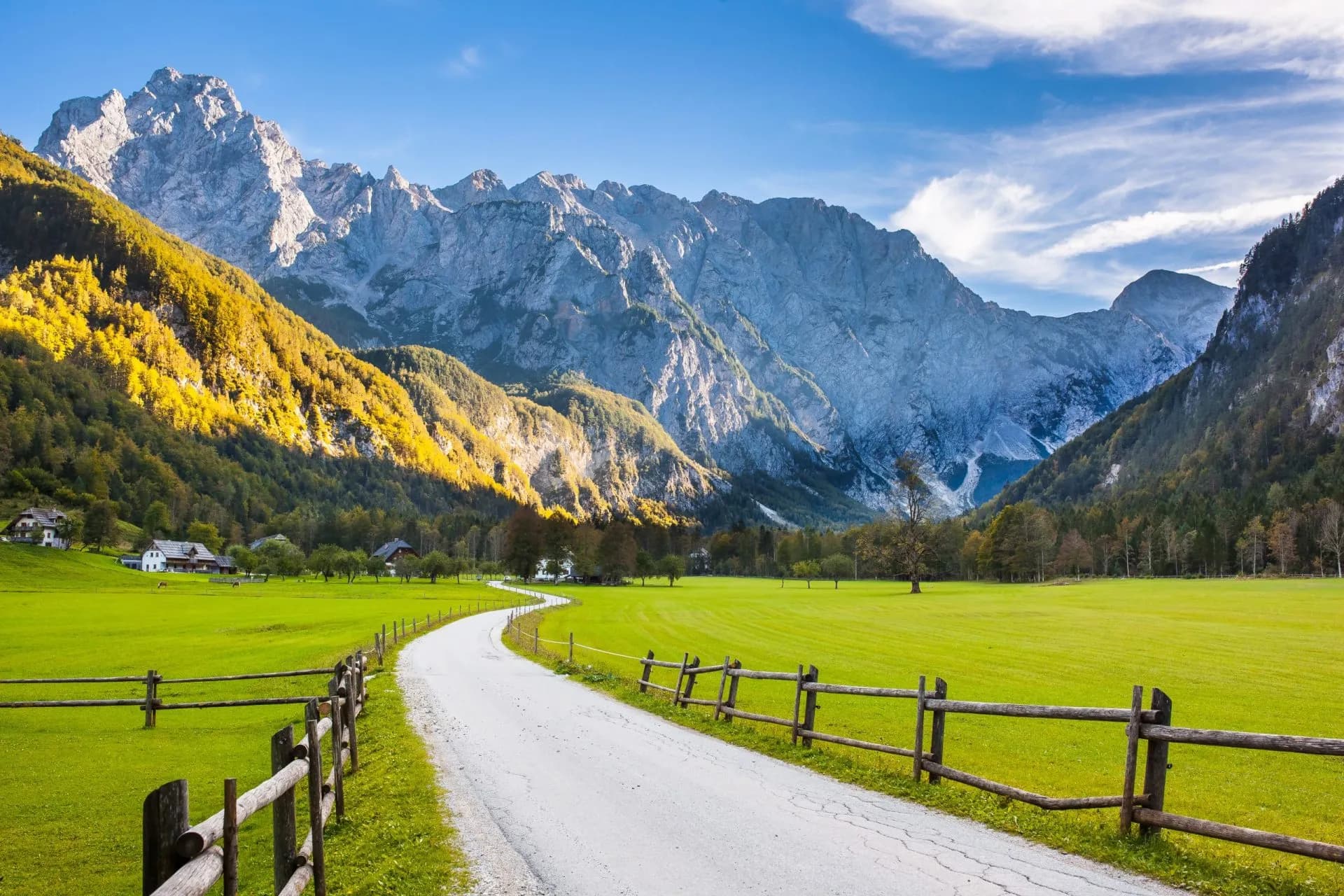 Winding road through Logar Valley, Slovenia, past green fields and tall, rocky mountains.