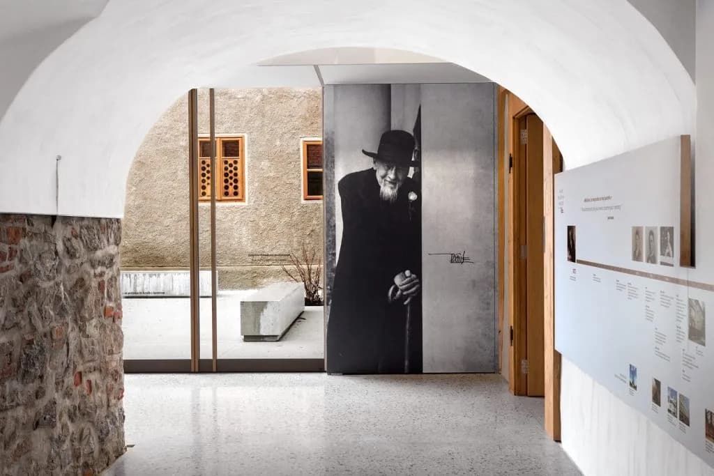 Interior view of Plečnik House entrance with stone wall, timeline display, and portrait of a man.