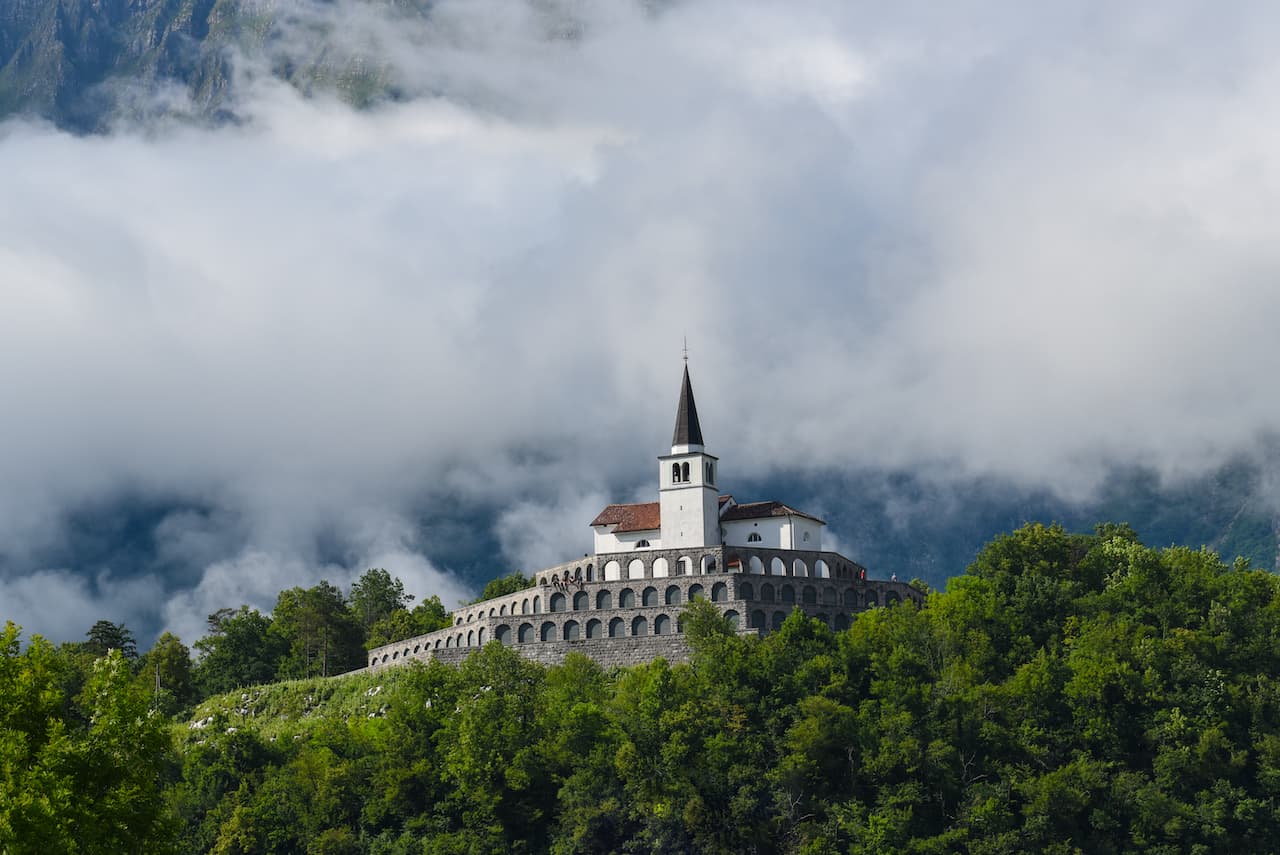 WWI memorial church on a forested hill emerging from low clouds in Kobarid.