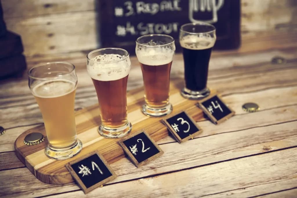 Beer tasting flight with four different beers on a wooden board with numbered chalk signs.