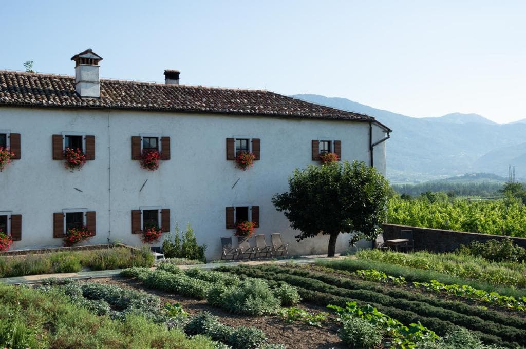 White farmhouse with flower boxes, herb garden, and mountains in background