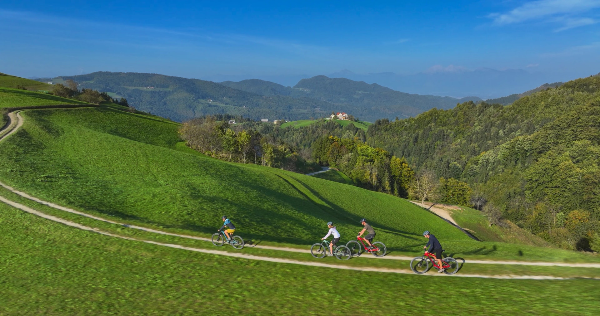 A group of friends ride their modern electric bikes along a scenic gravel path in the picturesque green hills of Slovenia