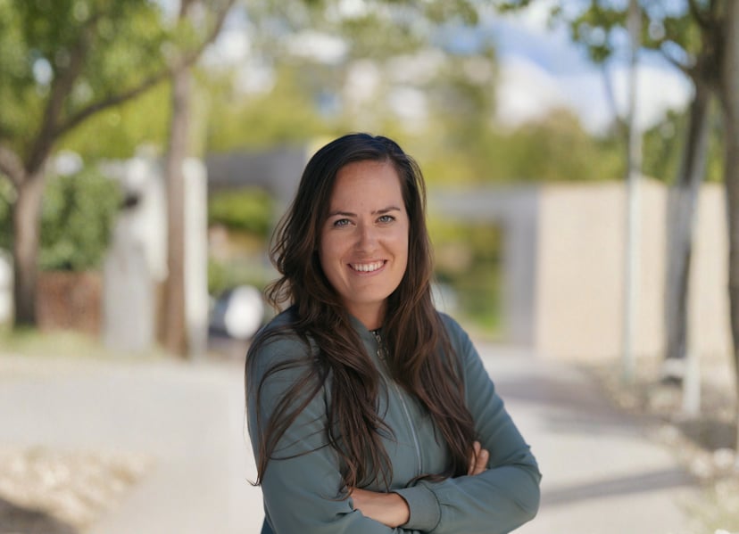Smiling woman with long brown hair standing outdoors with arms crossed.