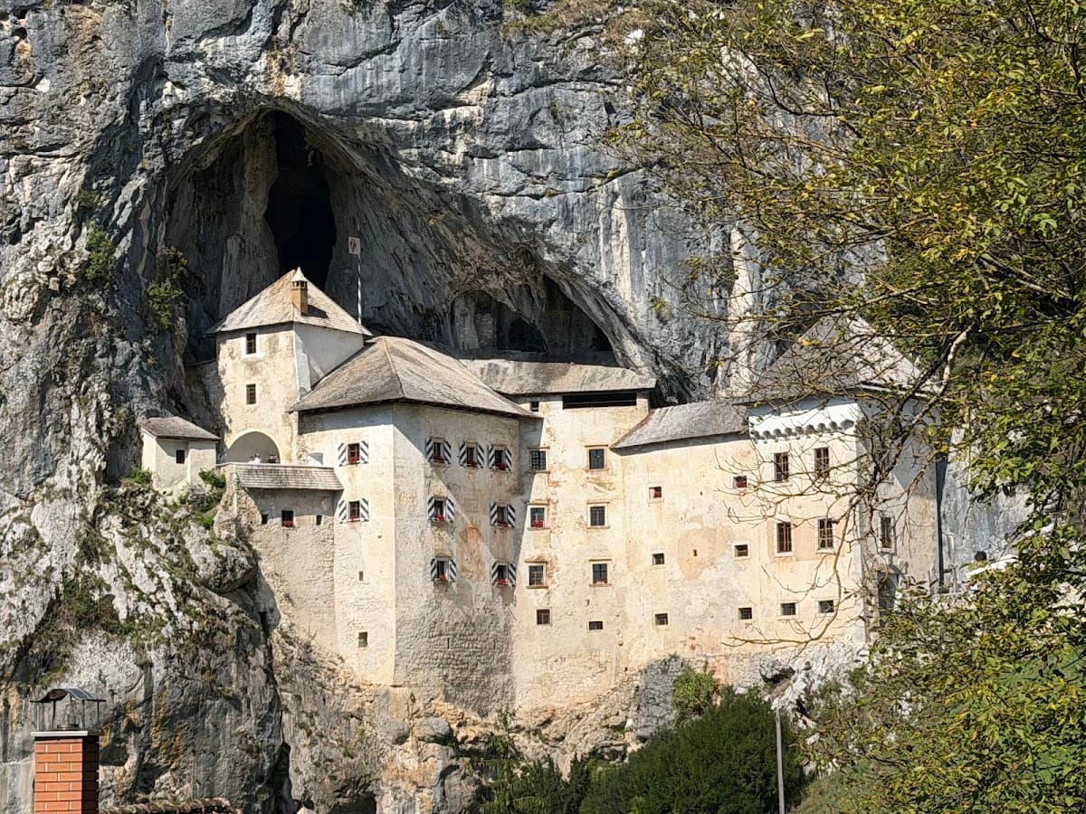 Historic medieval castle built into a cliffside cave mouth with rocky mountain backdrop