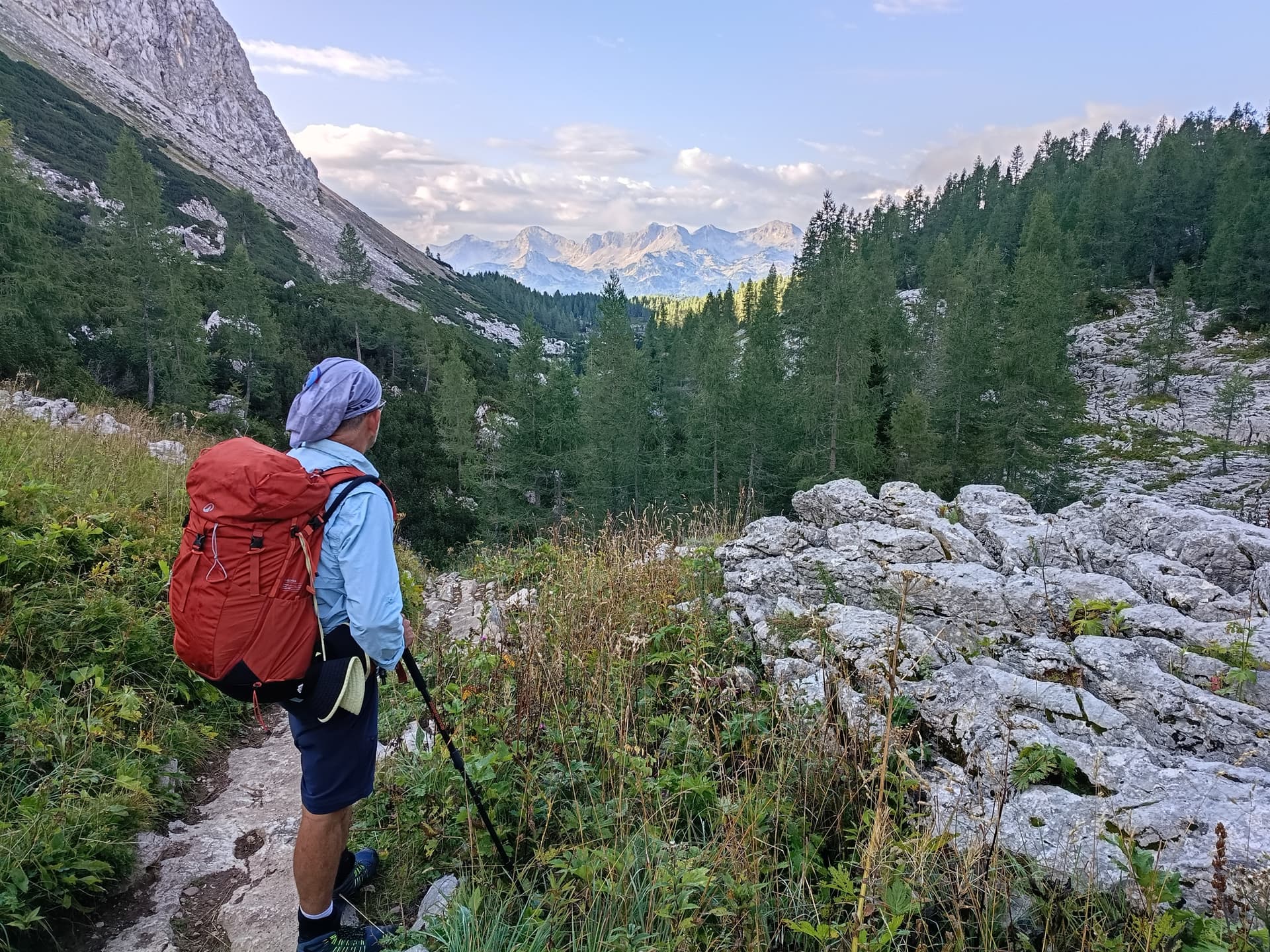 Hiker with red backpack on limestone trail in the Julian Alps