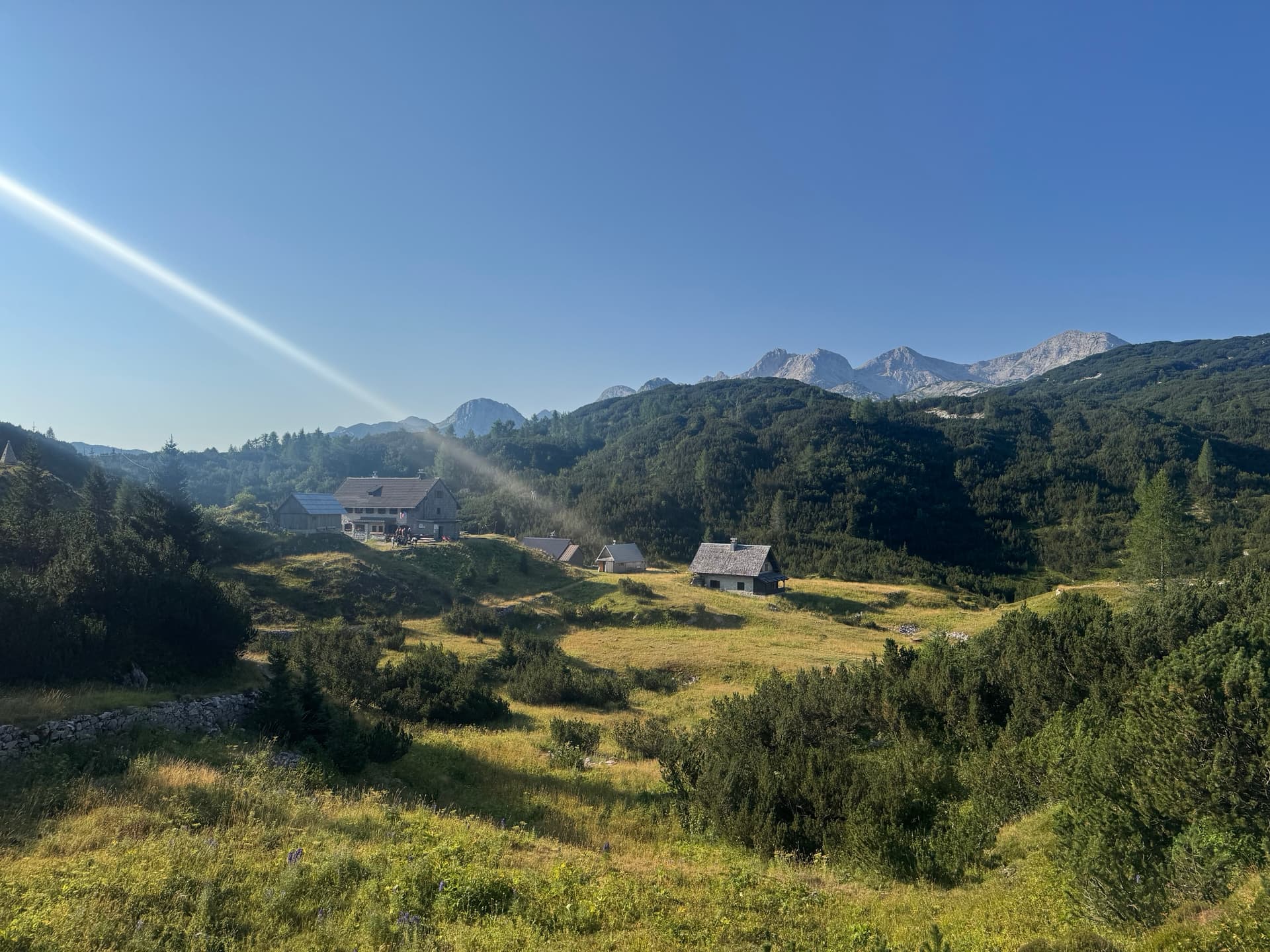 Morning sun illuminating alpine plateau with stone houses and mountain peaks