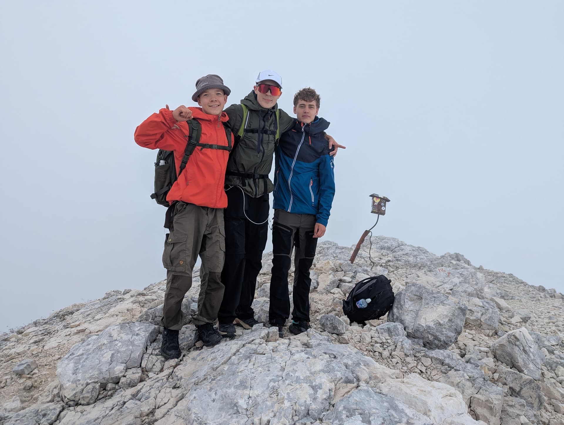 Three hikers standing together on a rocky mountain summit in foggy weather