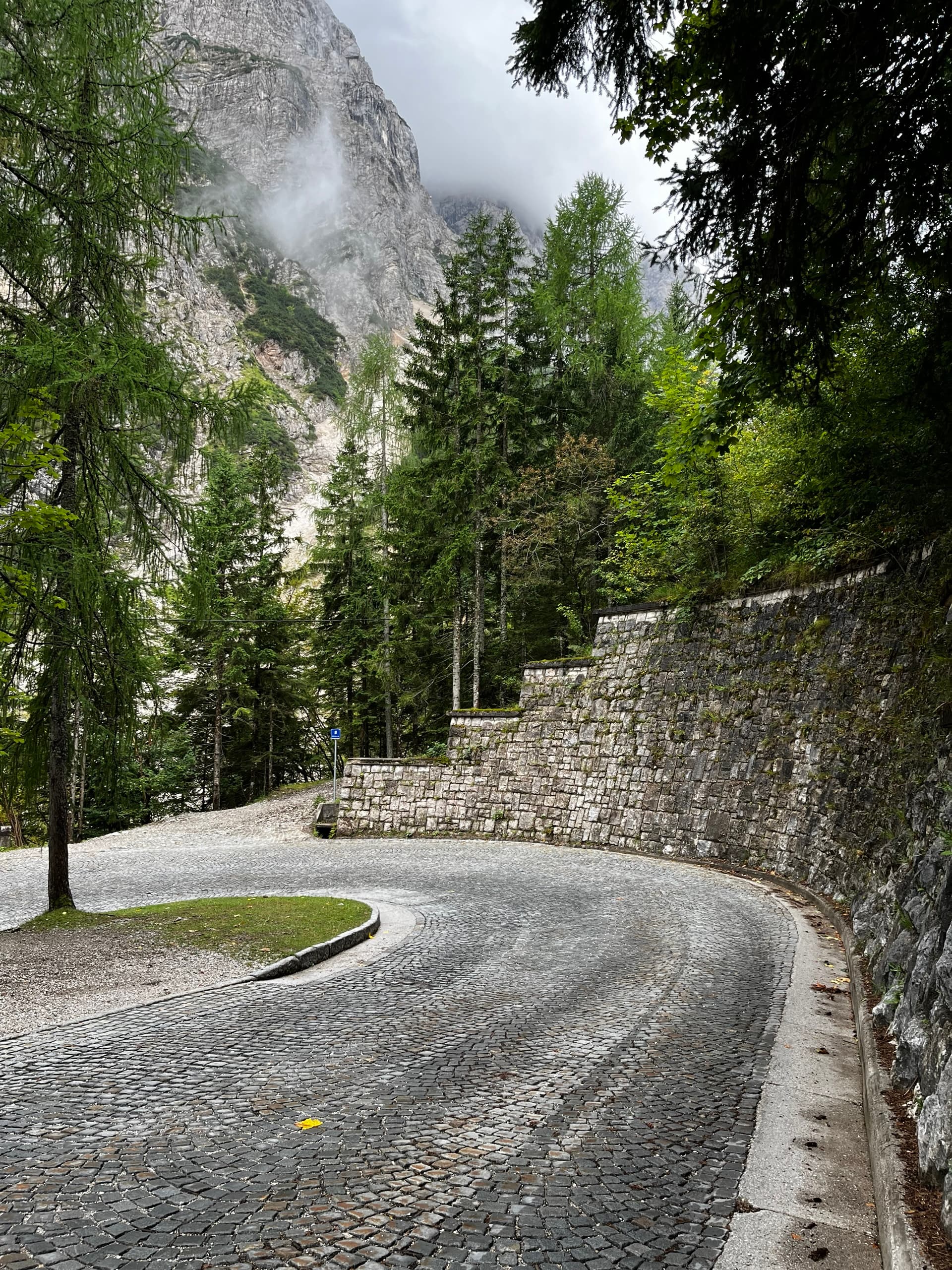 Cobbled hairpin turn on mountain pass with stone retaining wall and pine trees